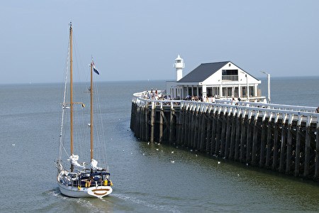 a sailboat passes by the eastern jetty with a white brasserie