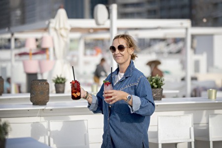 woman carries 2 cocktails in the white interior of a beach bar