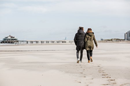 Couple in winter clothing walks along the beach towards the Pier